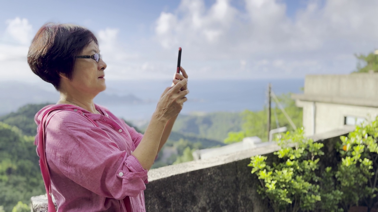 一位亚洲老妇人正在用她的手机拍摄台湾旅游景点九分的美景。视频下载