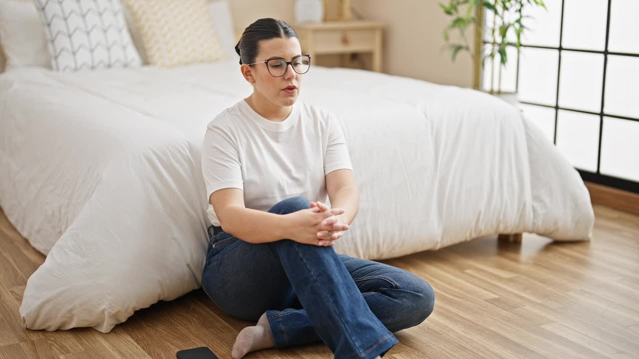 年轻漂亮的西班牙女人坐在地板上看着卧室里的悲伤视频素材