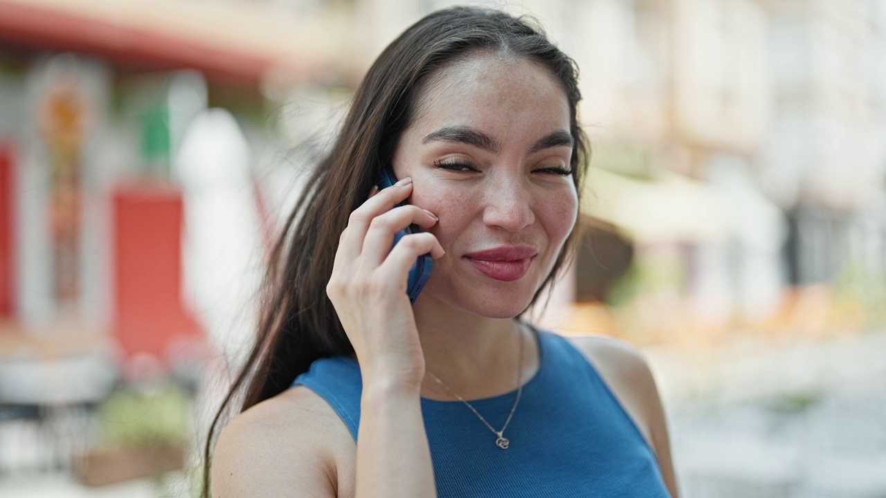 年轻美丽的西班牙女子微笑着自信地在街上用智能手机聊天视频素材