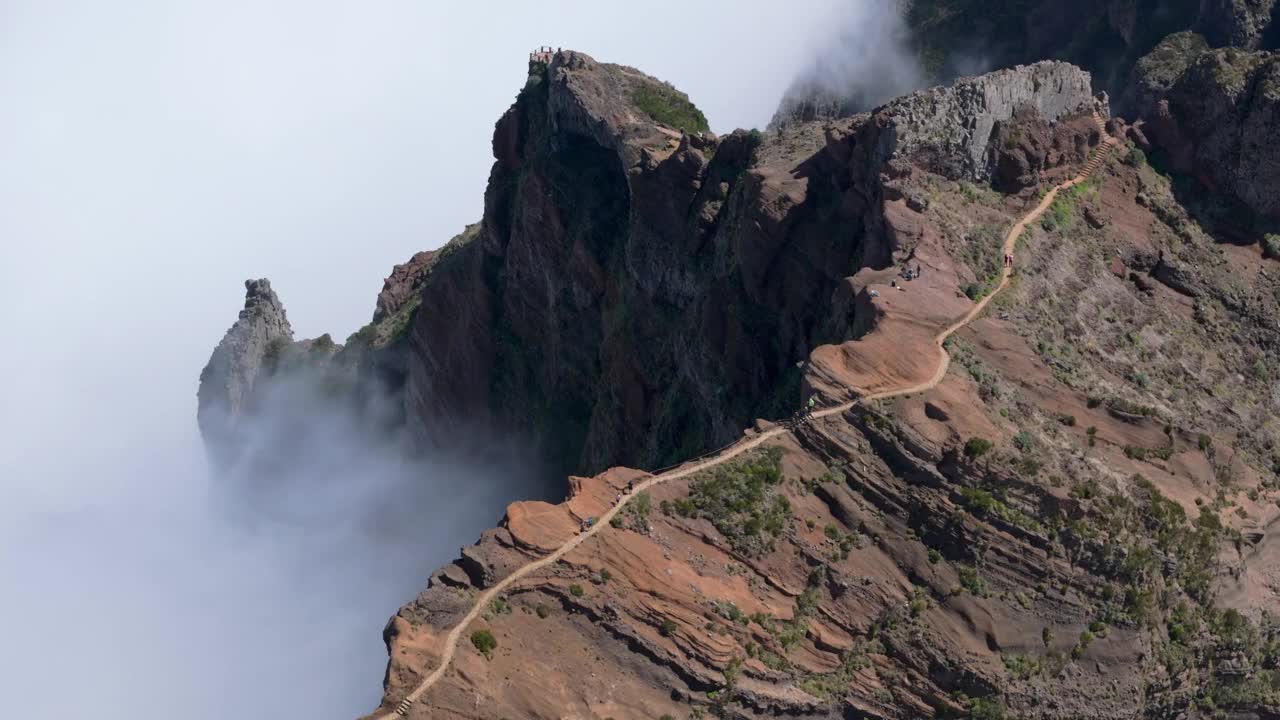 徒步旅行著名的Pico Areeiro到Pico Ruivo山徒步旅行在马德拉岛，葡萄牙，无人机视图。人们走在云雾缭绕的陡峭山脊上狭窄的小路上。视频素材