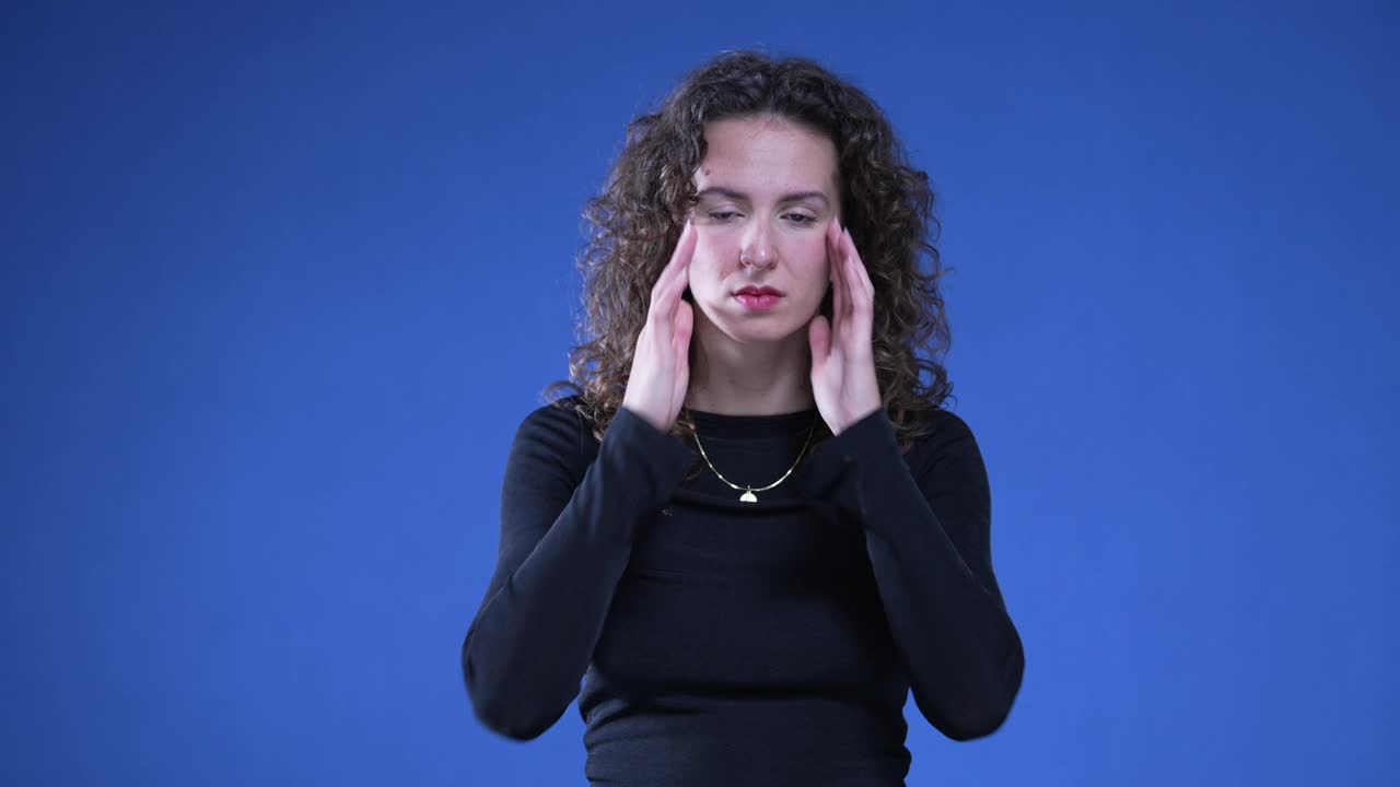 压力大的女人用手摸太阳穴平静自己，感到痛苦和头痛。与精神焦虑作斗争的人站在蓝色背景上视频素材