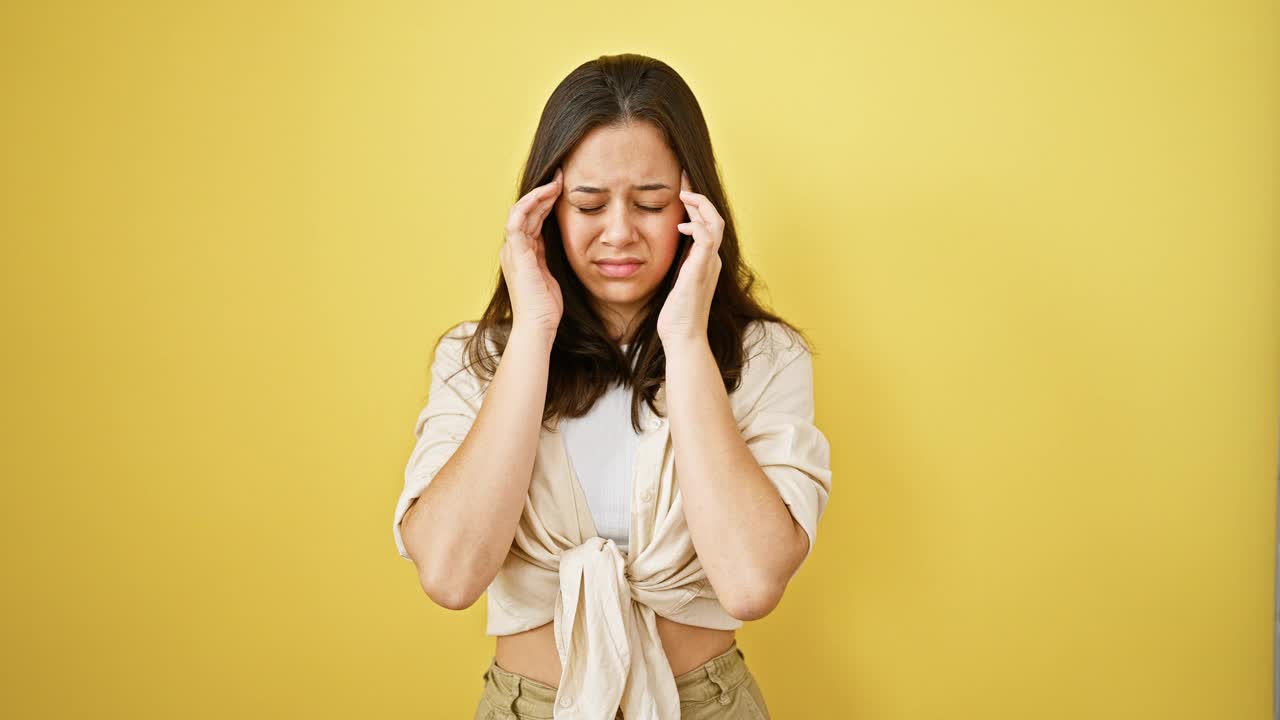 年轻美丽的西班牙妇女患头痛孤立的黄色背景视频素材