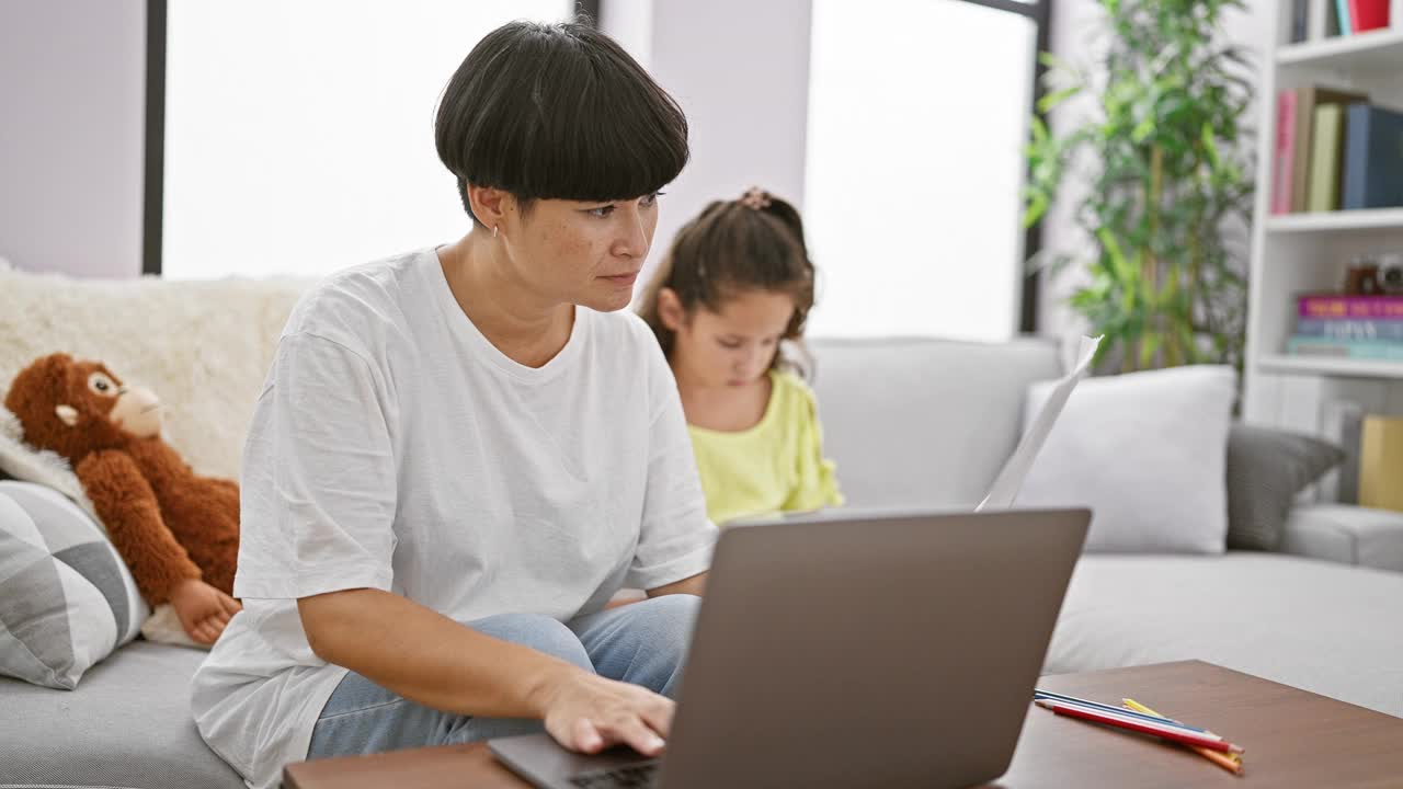 母女俩温馨的学习，一起坐在舒适的沙发上，沉浸在远程办公和网上作业中，在家里创造一个美丽的室内家庭时刻。视频素材