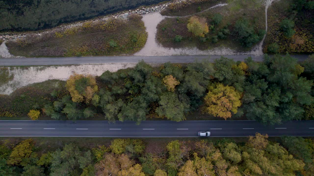 一辆车在与人行道和秋天的树木平行的道路上的俯视视图。视频素材