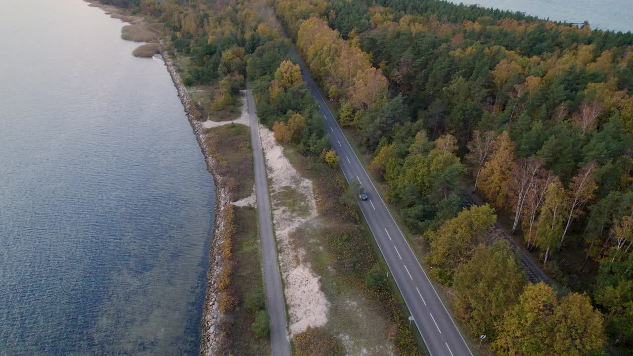 汽车行驶在沿海的道路上，秋天的树叶和黄昏平静的大海。视频素材