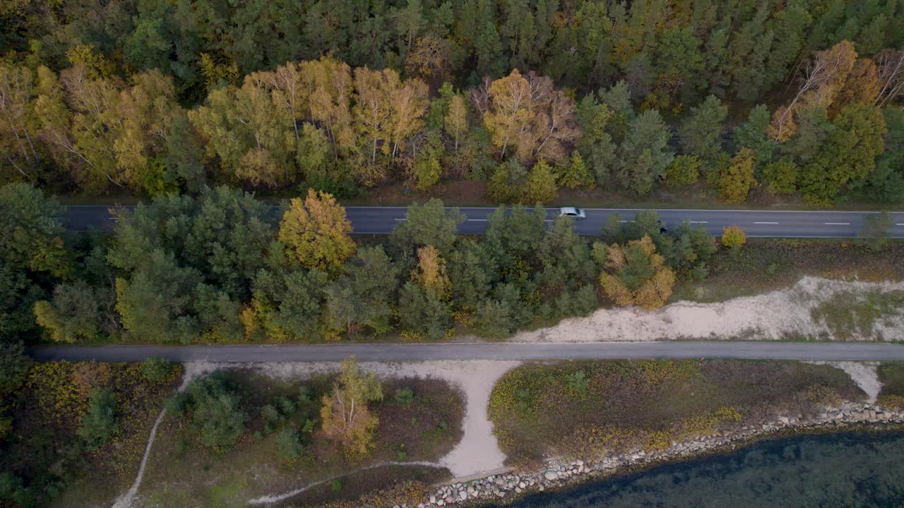 航拍的一条安静的道路，在一片秋叶茂密的森林和布满岩石的海岸线之间视频素材