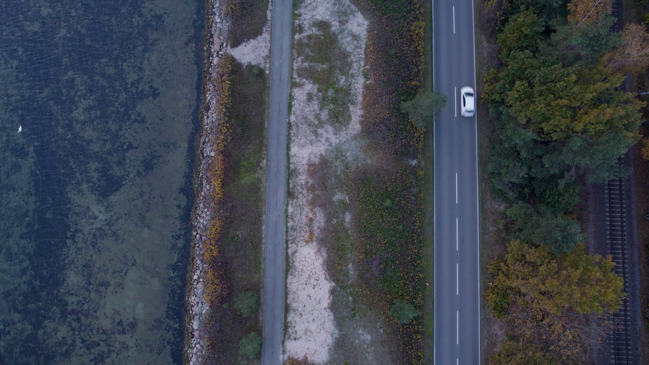 一条双车道公路的俯拍照片，车辆行驶在一片沙地和一片秋叶茂密的森林之间。视频素材