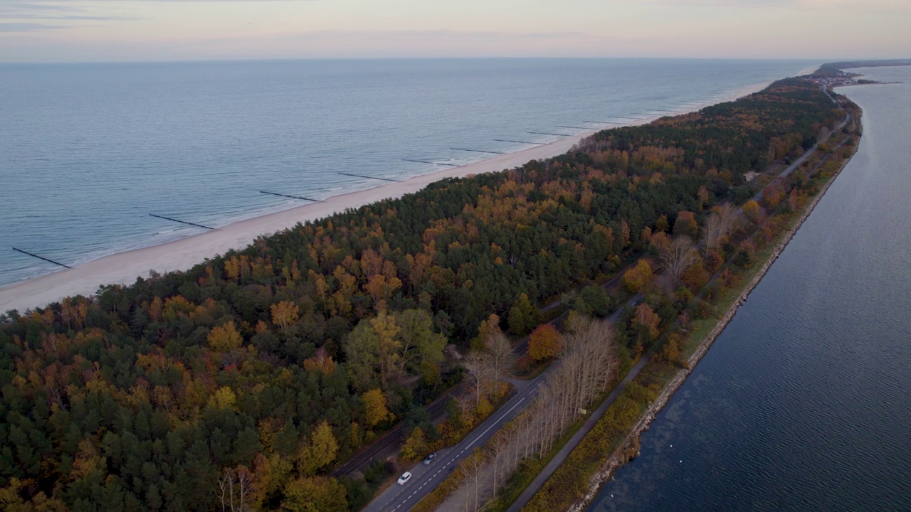 黄昏时，一条沿海道路的鸟瞰图，一边是相邻的海滩和大海，另一边是秋天的森林——波兰库兹尼察视频素材