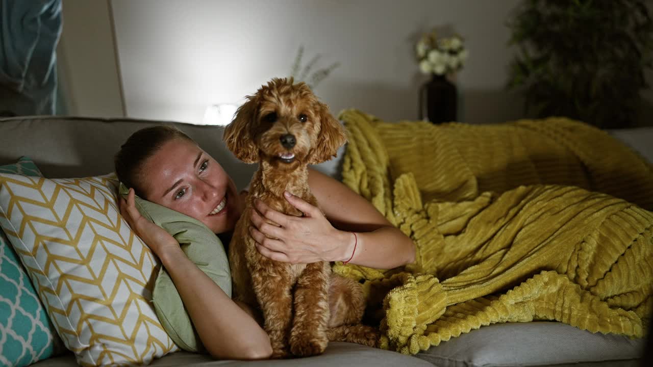 年轻的白种女人带着小狗躺在家里的沙发上视频素材