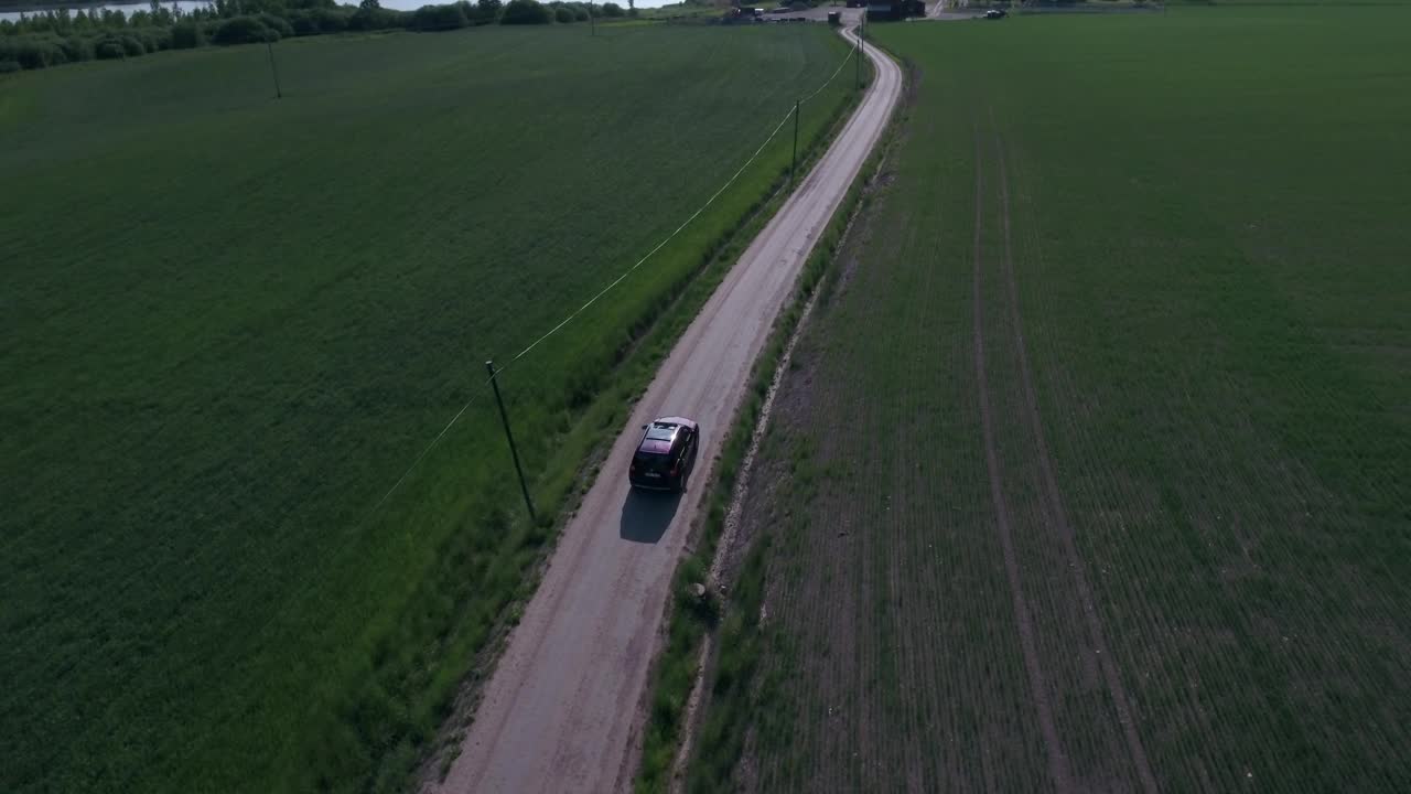 在阳光明媚的日子里，汽车在湖边的绿色景观之间的道路上移动的航拍向前拍摄-林德斯堡，瑞典视频素材