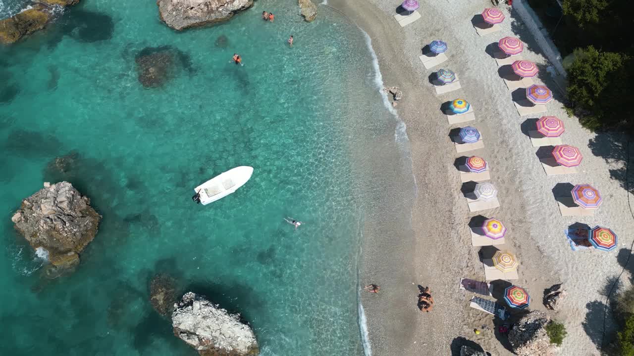 从上到下的无人机升起，海浪轻轻地拍打着海岸线，岸边有伞和船视频素材