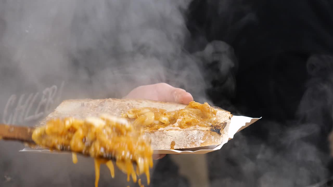 男子将烤好的洋葱铺在一大片面包上，波兰传统美食节市场摊位的特写细节，食物准备，买卖传统小吃和当地菜肴的概念视频下载