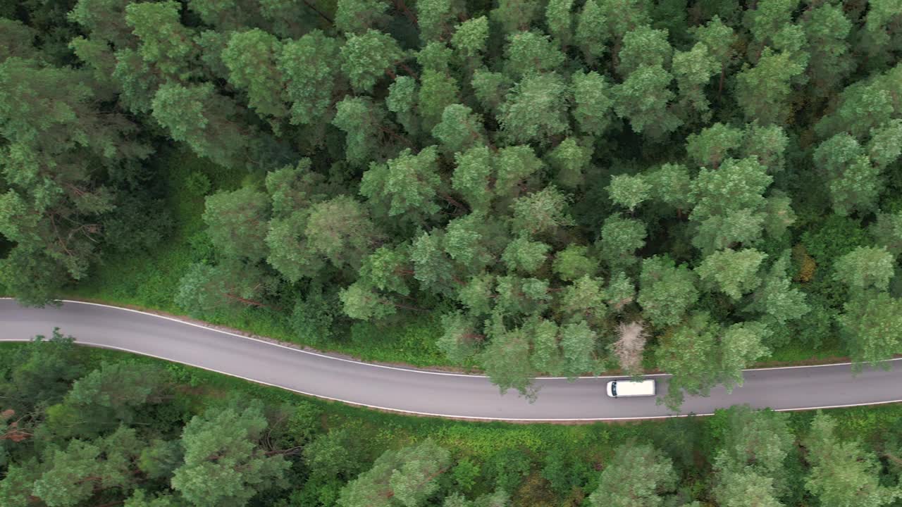 鸟瞰图夏日，白色轿车行驶在柏油路上，穿过广阔的森林。汽车在松林道路上行驶的航拍照片。穿越森林的公路旅行。风景优美的夏季景观。视频素材