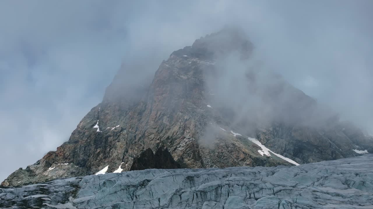 在阳光明媚的夏日，意大利Valmalenco，无人机飞过费拉里亚冰川，背景是云层笼罩的雄伟的岩石山。空中侧视频素材