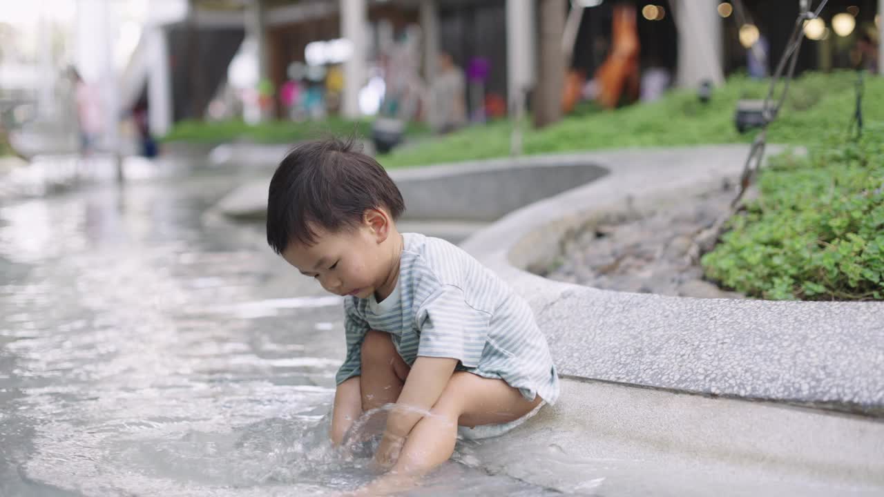 可爱的小男孩在公园操场上玩水。视频素材