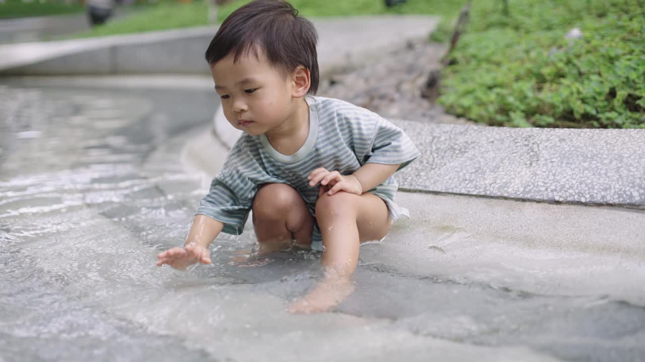 可爱的小男孩在公园操场上玩水。视频素材