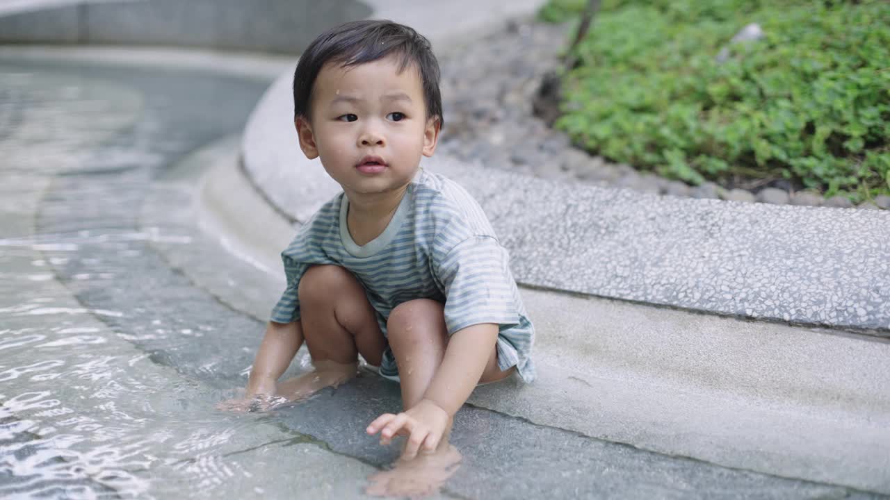 可爱的小男孩在公园操场上玩水。视频素材