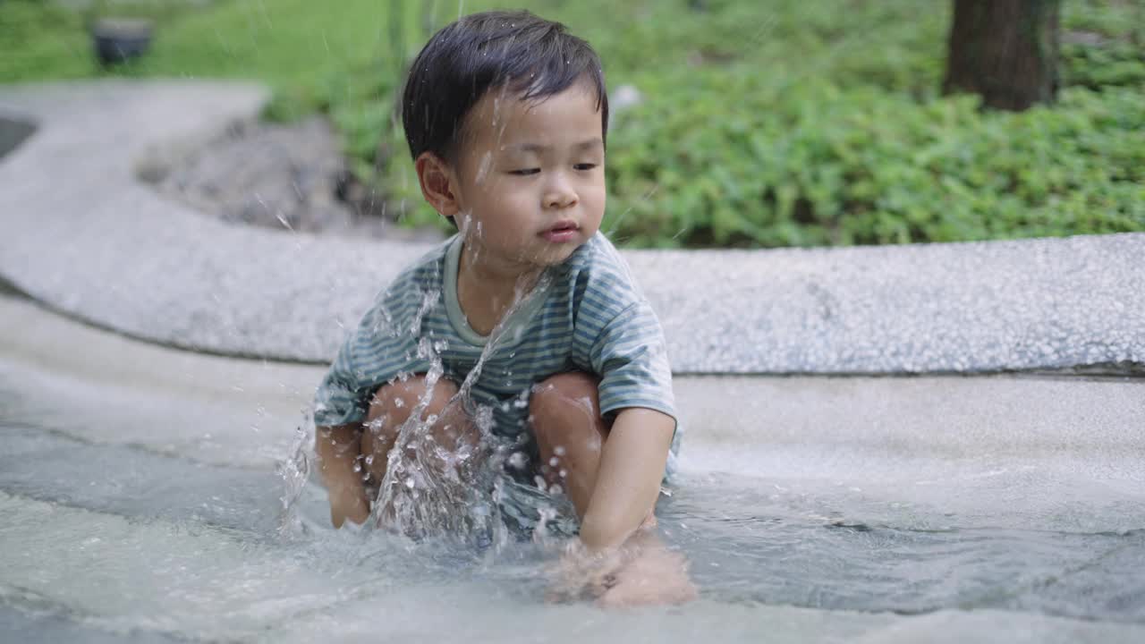 可爱的小男孩在公园操场上玩水。视频素材