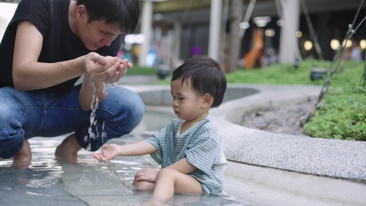 可爱的小男孩和他的爸爸在公园操场上玩水视频素材