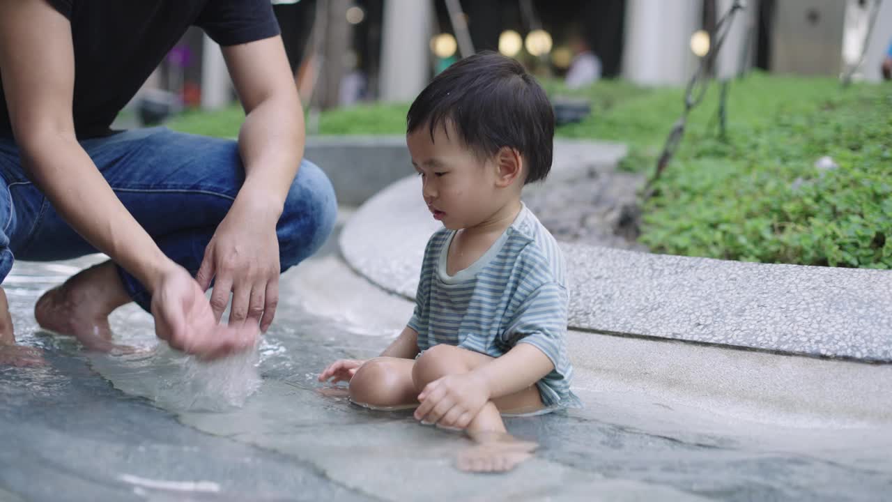 可爱的小男孩和他的爸爸在公园操场上玩水视频素材