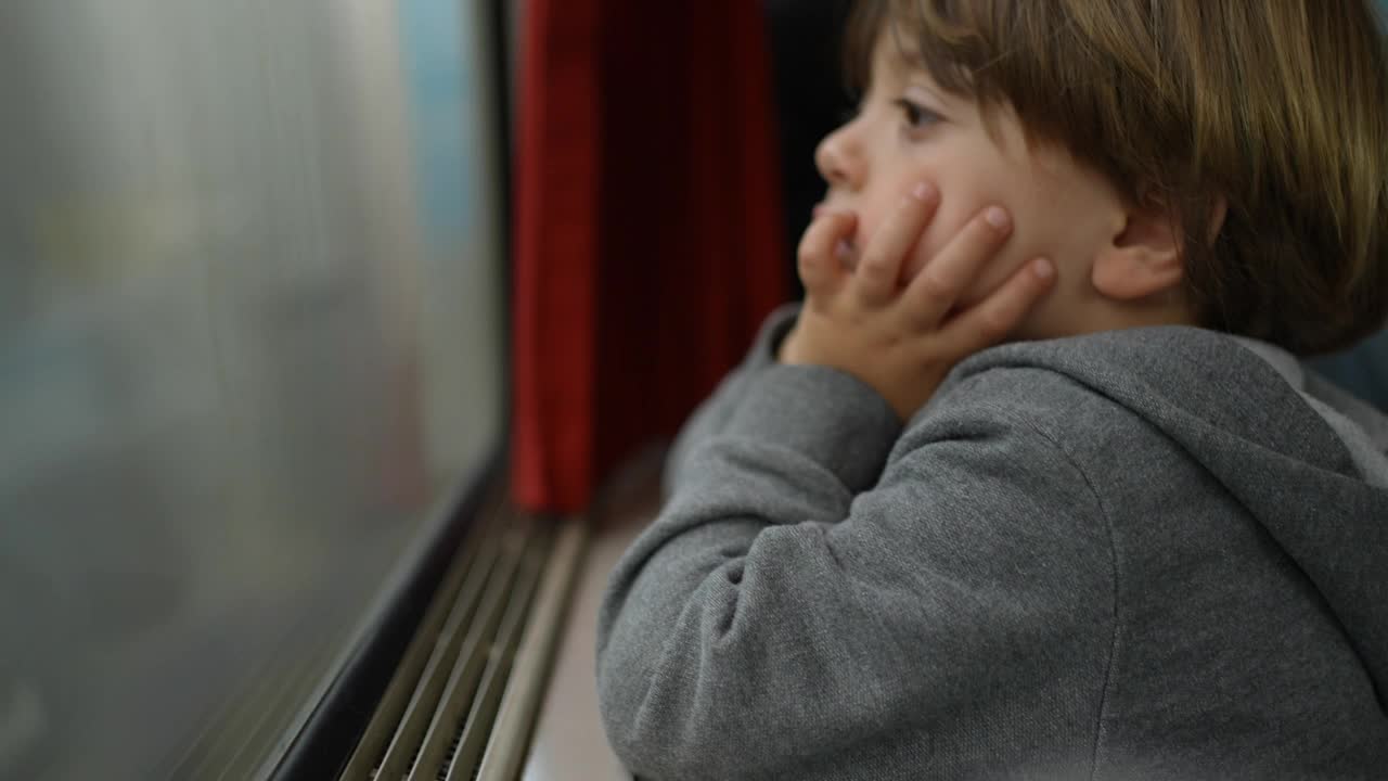 乘火车旅行的乘客小孩在高速运输中盯着平行列车经过。体贴的小男孩，双手托着下巴，在旅行时做白日梦视频素材