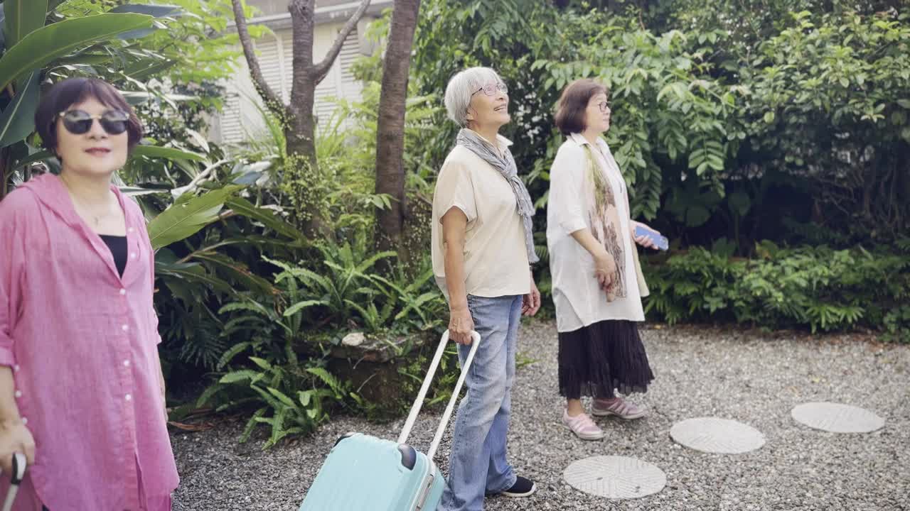 三个年近七十的亚洲老妇人一起旅行。他们拉着带轮子的行李箱，一起来到了民宿的门口。他们站在院子里，欣赏着他们接下来几天要住的旅馆。视频下载