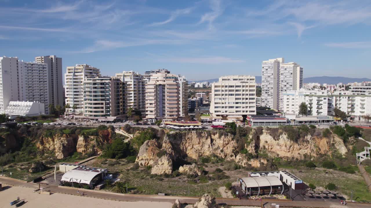 热门旅游胜地普拉亚达罗查沙滩和悬崖峭壁，在波尔蒂茂住宅建筑，向后飞视频素材