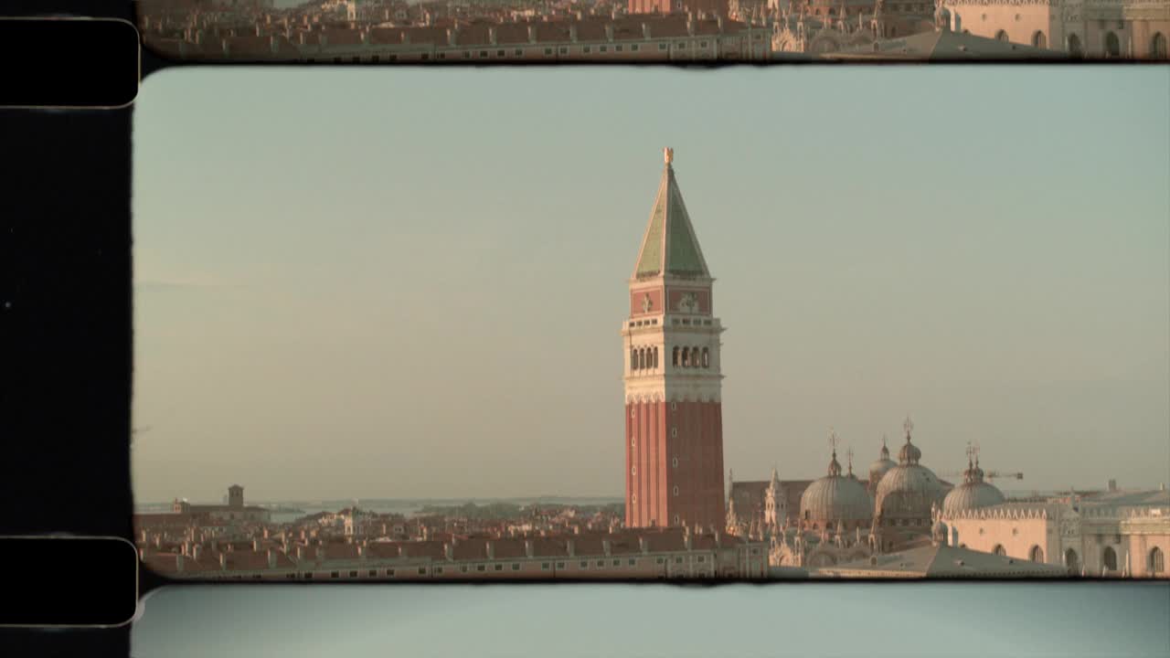 阳光下的意大利威尼斯屋顶鸟瞰图，远处是圣马可钟楼和大教堂。4 k视频下载