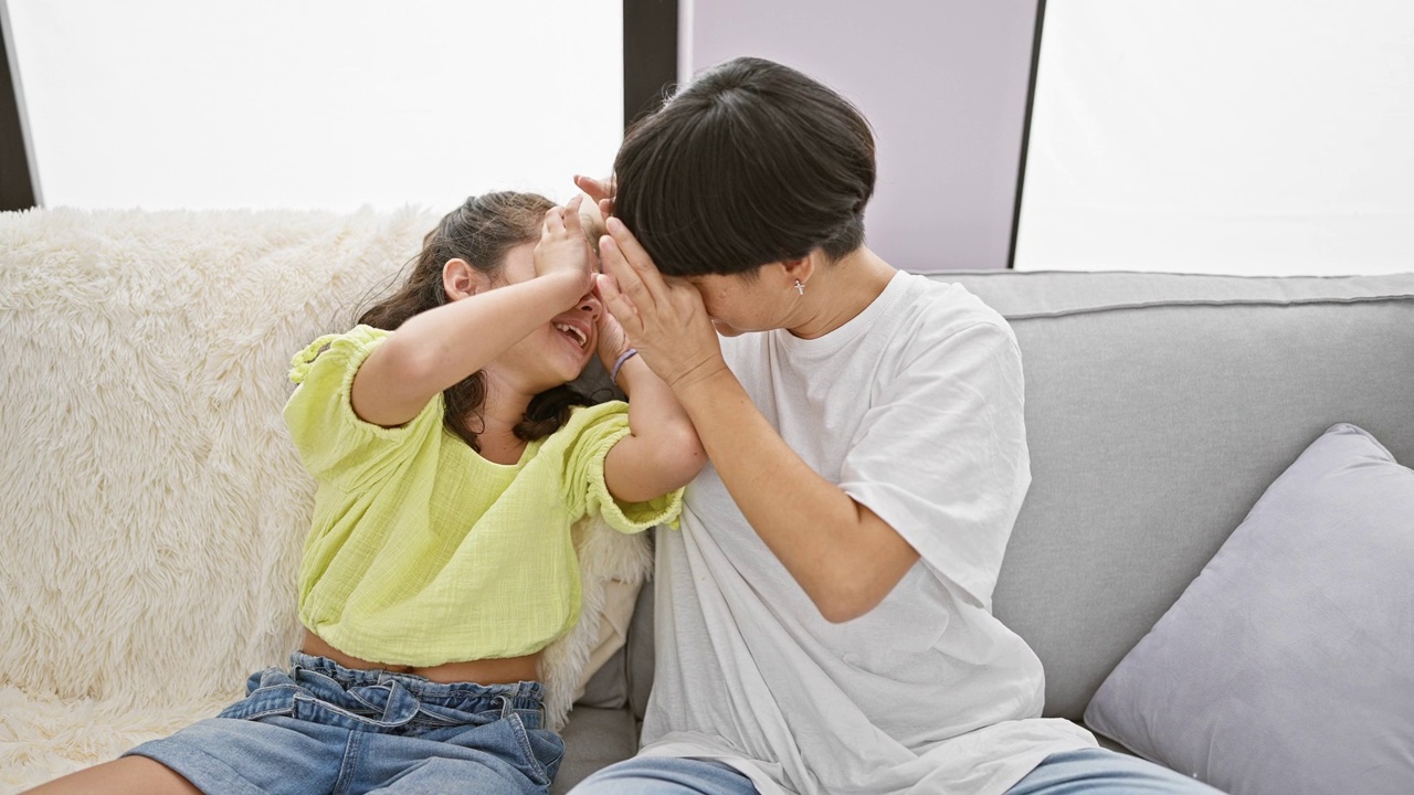 幸福的母女俩坐在家里的沙发上，自信地用手指做着凉爽的眼镜手势，同时分享着一个快乐、可爱的时刻视频素材