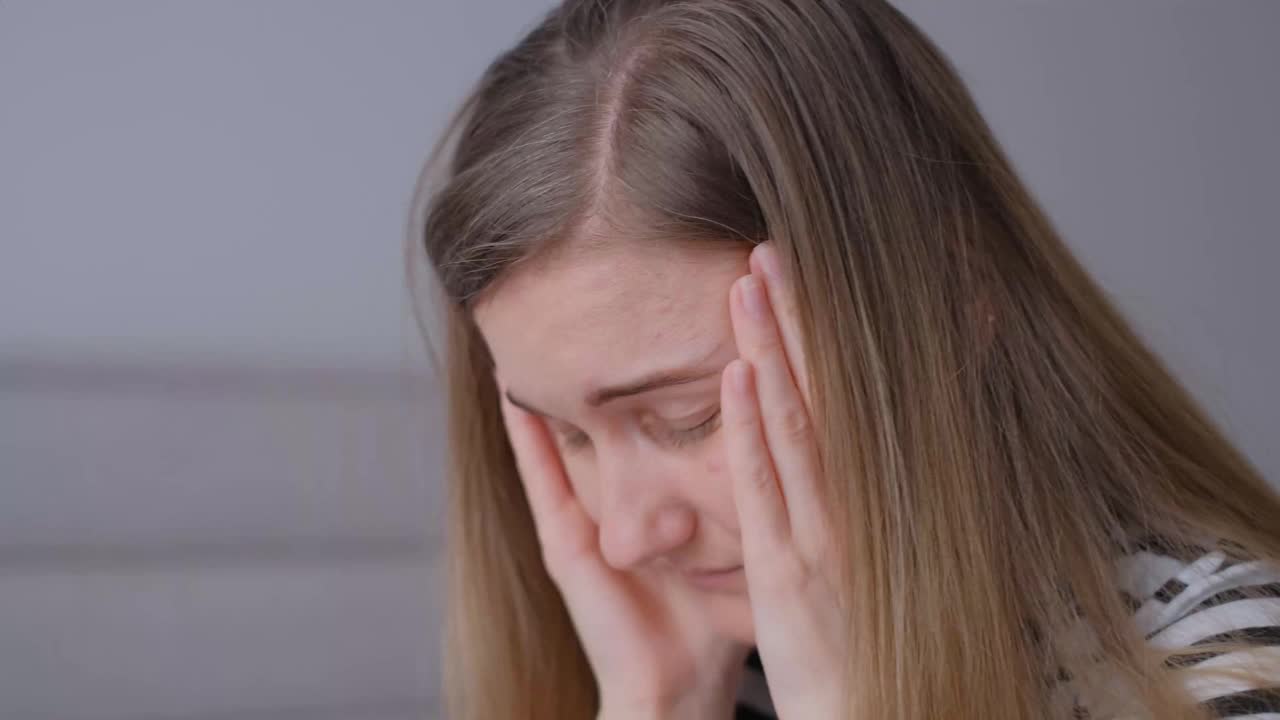 一个年轻女子闭着眼睛遭受头痛的特写。女孩忧心忡忡，倍感压力。视频素材