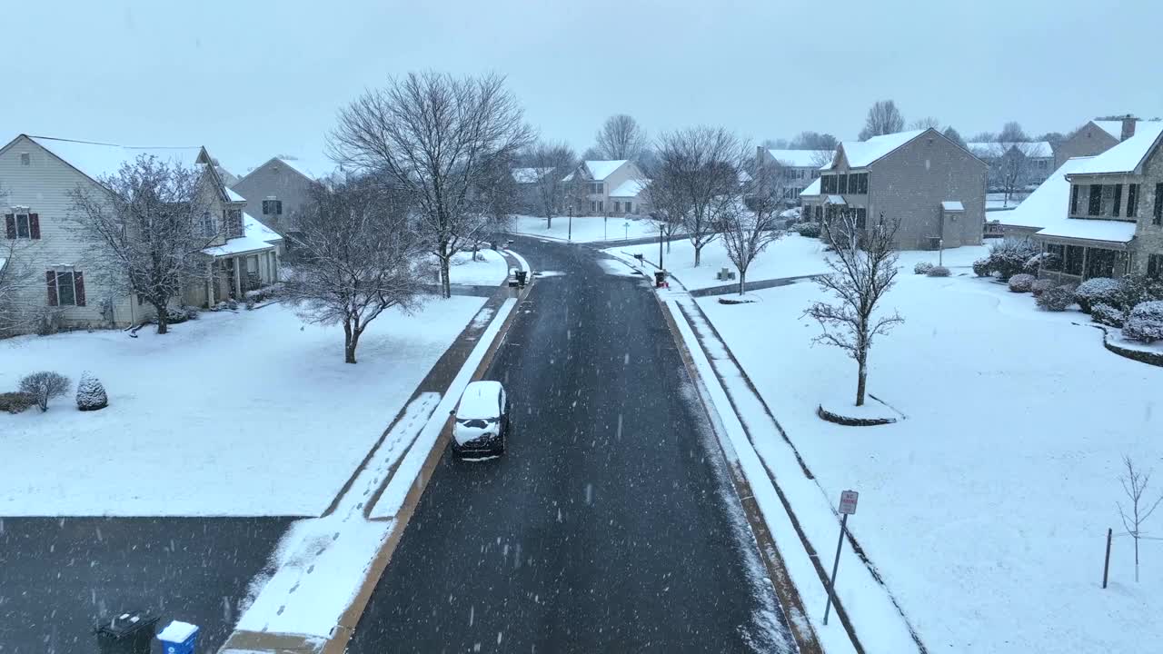 冬天的郊区街道:白雪覆盖的草坪和光秃秃的树木，弯曲的道路两旁排列着现代化的房屋。空中无人机在小雪中拍摄。视频素材