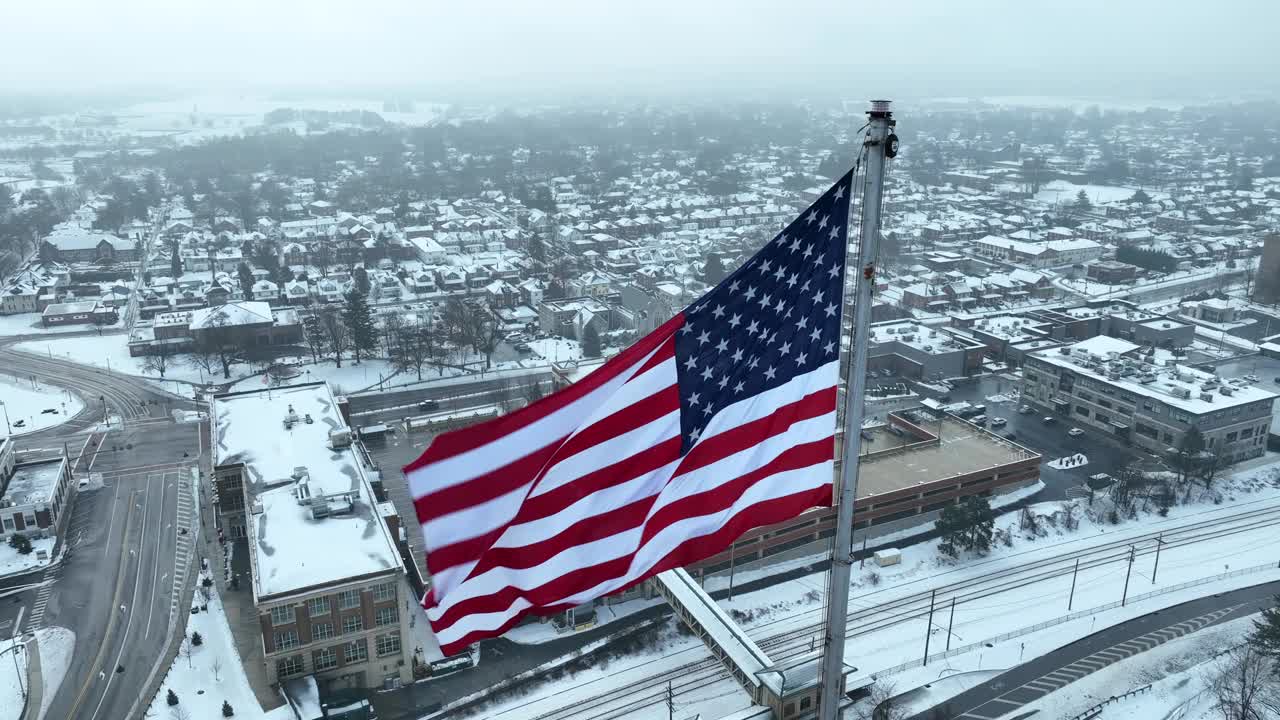 美国国旗在郊区雪景上飘扬的航拍近景。美国小镇主题。视频素材