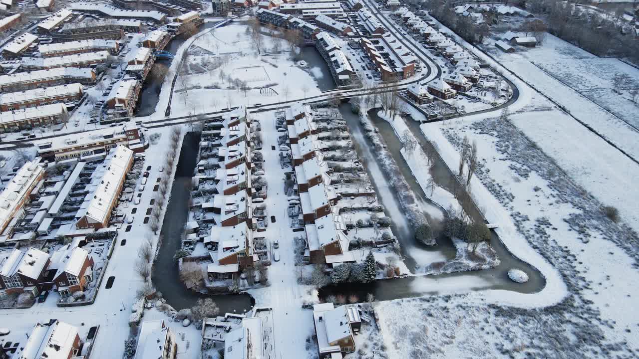 美丽的航拍，一个下雪的郊区社区，有一个被雪覆盖的公园和结冰的池塘视频素材