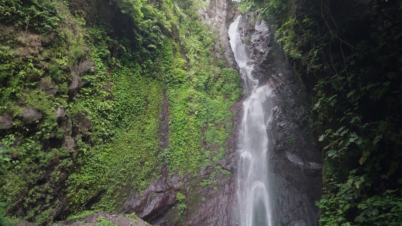 瀑布(Yeh Mempeh或飞瀑)在Tejakula村，Buleleng，巴厘岛-隐蔽的瀑布被雨林包围，悬崖上长满了绿色的热带植物视频素材