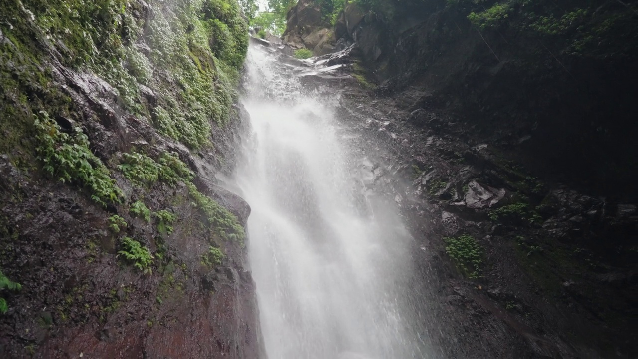 瀑布(Yeh Mempeh或飞瀑)在Tejakula村，Buleleng，巴厘岛-隐蔽的瀑布被雨林包围，悬崖上长满了绿色的热带植物视频素材