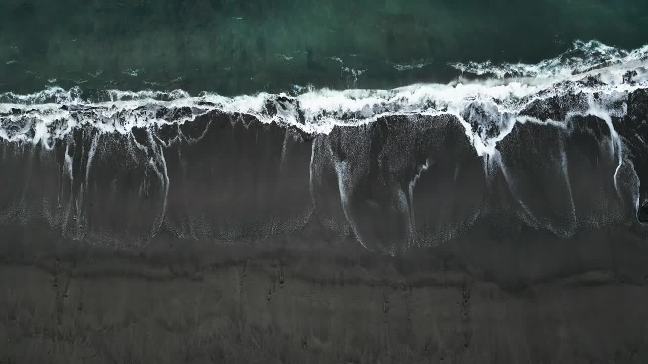 海浪拍打着黑色的沙滩，白色的泡沫与黑暗的海岸线形成鲜明的对比，鸟瞰图视频素材