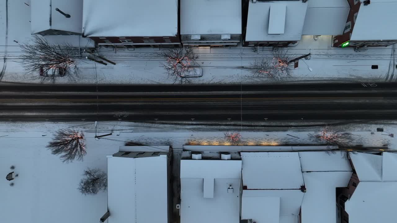 大雪覆盖了美国小镇的街道，街道上挂满了节日的彩灯和交通。黄昏时从空中俯瞰的卡车照片。视频素材