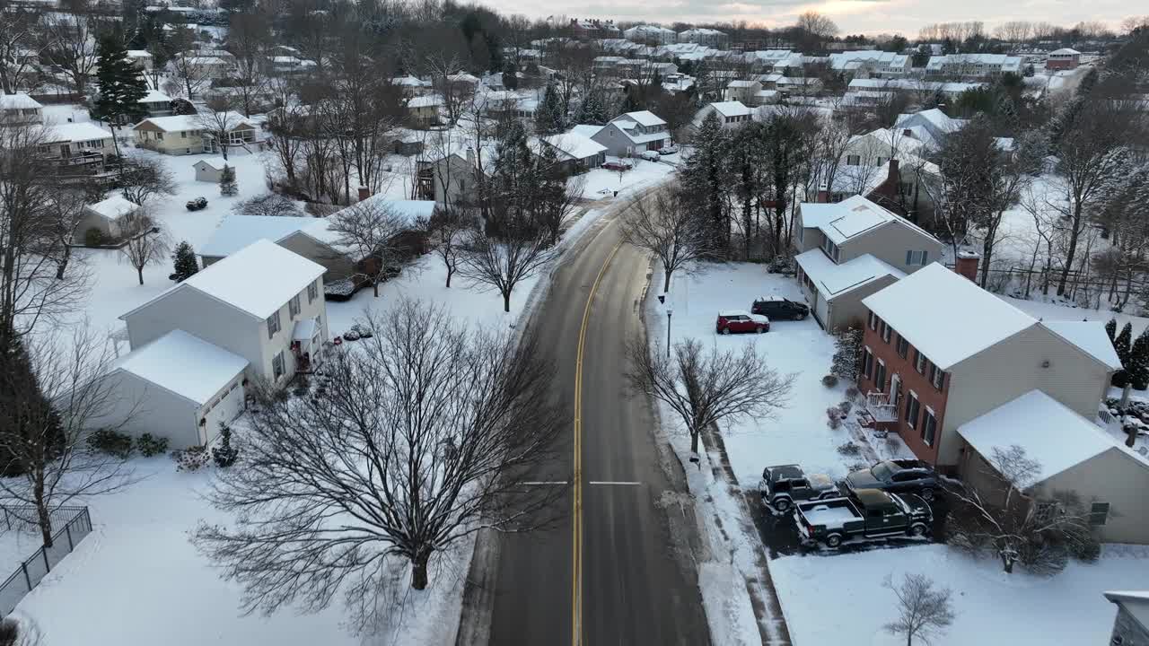 积雪覆盖的美国郊区。白雪皑皑的住宅区街道上有房屋、光秃秃的树木和日落时停着的汽车。视频素材