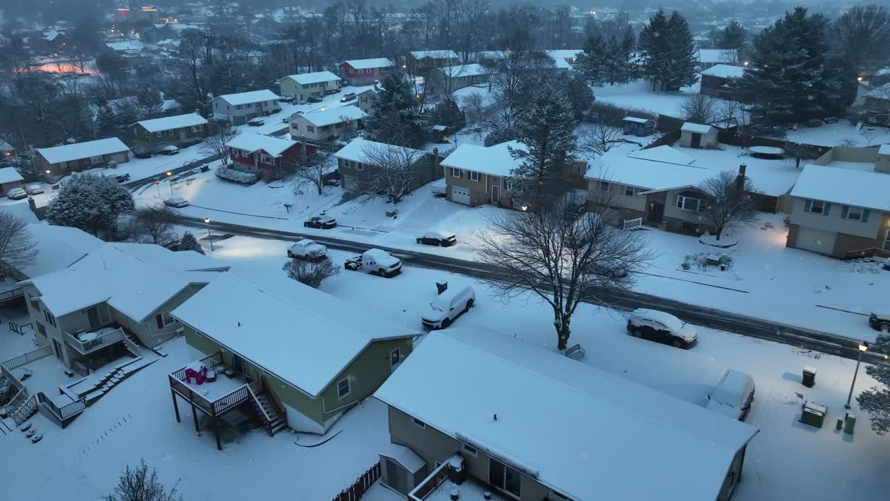 黄昏降临在一条白雪皑皑的住宅区街道上，街道上有房子和停着的汽车。美国古色古香的小镇附近飘起了小雪。视频素材