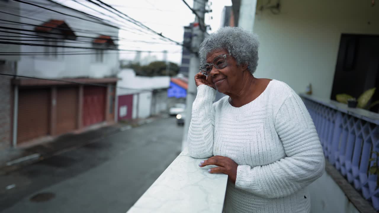 一位南美老妇人从住宅阳台观察社区。80年代的老人带着快乐的表情俯视城市街道视频素材