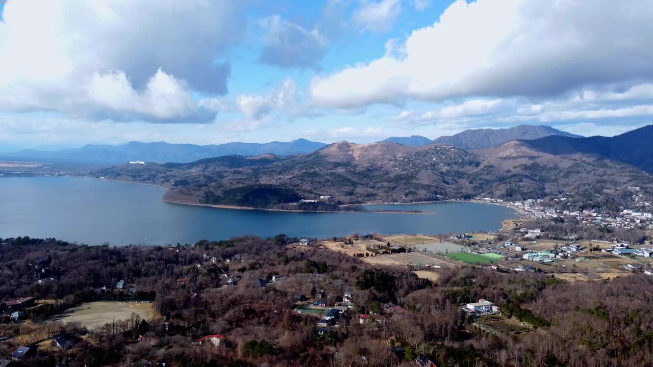 在多云的天空下，一个宁静的湖泊旁边是一个小镇和山脉，白天，鸟瞰图视频素材