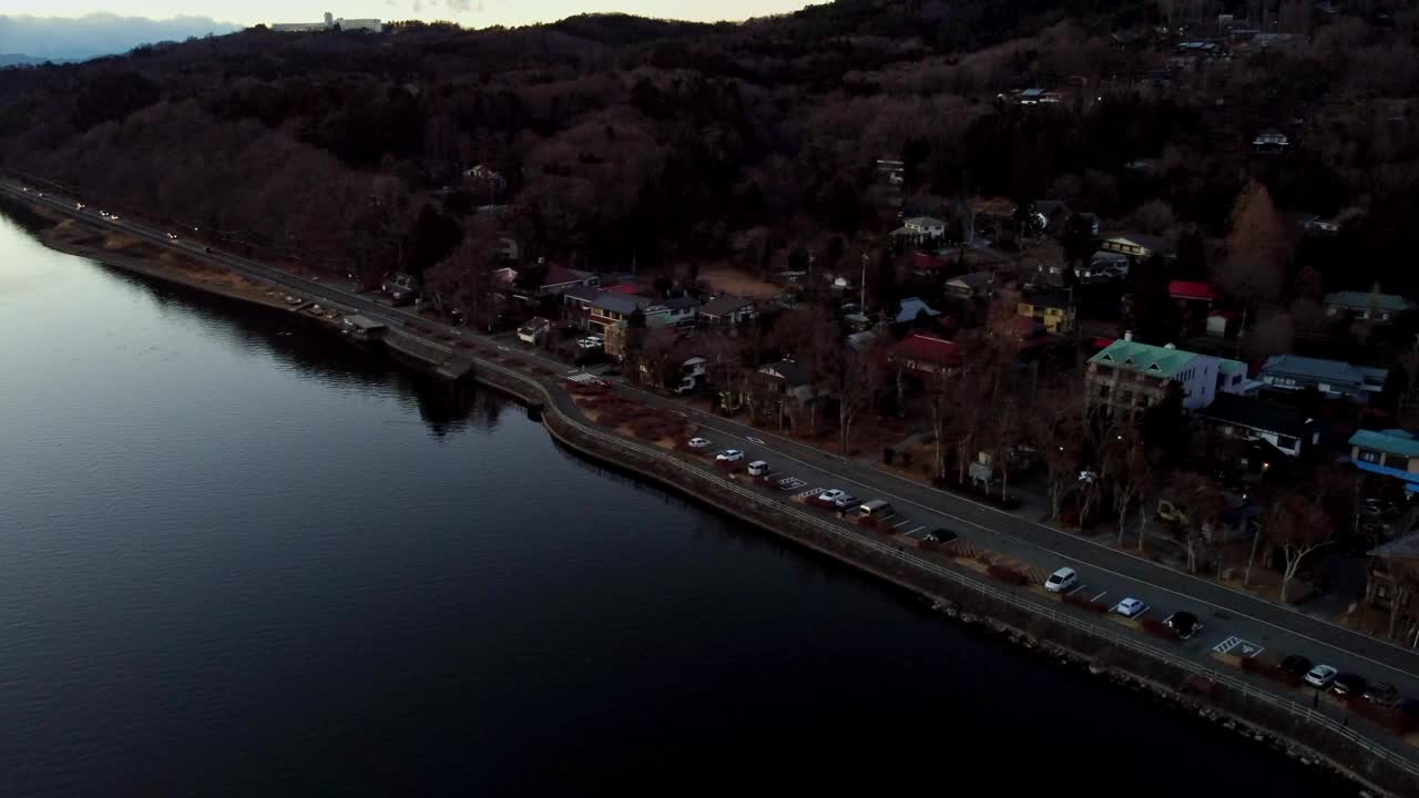 暮色笼罩在一条宁静的河流上，毗邻的道路和成排的汽车，住宅区绿树成荫视频素材