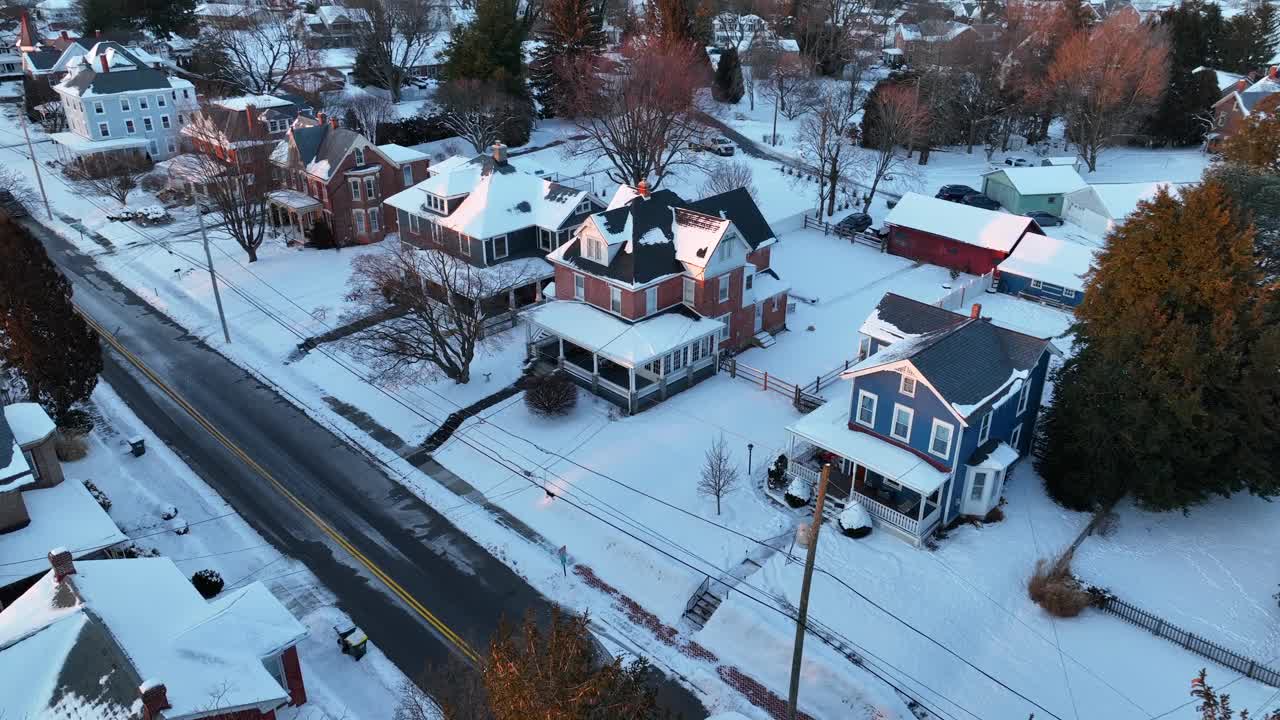 在下雪的冬日，小镇上的美国家庭和房屋。在美国，五彩缤纷的树木照亮了黄金时刻。空中倾斜的广角镜头。视频素材