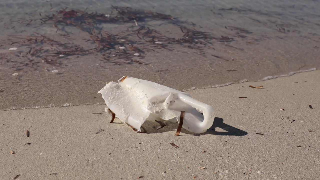 风化的塑料瓶散落在沙滩上，背景是海浪视频素材