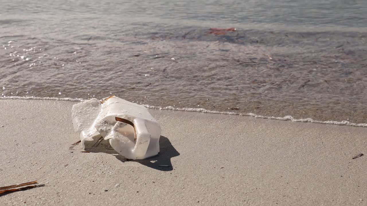 随着海浪的逼近，阳光沙滩上的塑料瓶污染，环境问题视频素材