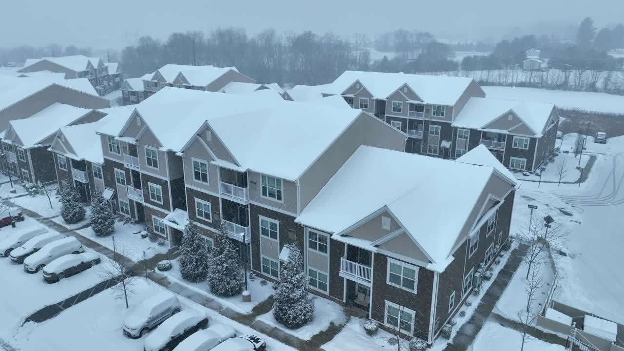 飘落的雪花覆盖了美国社区的屋顶和街道。道路上的积雪覆盖的汽车。下降无人机拍摄。视频素材