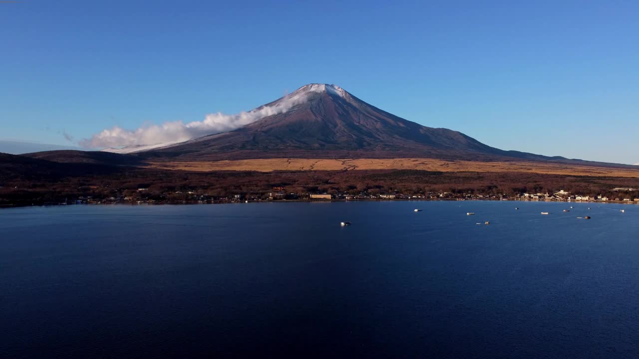 从平静的湖面上看富士山，黎明时分有船只，天空湛蓝视频素材