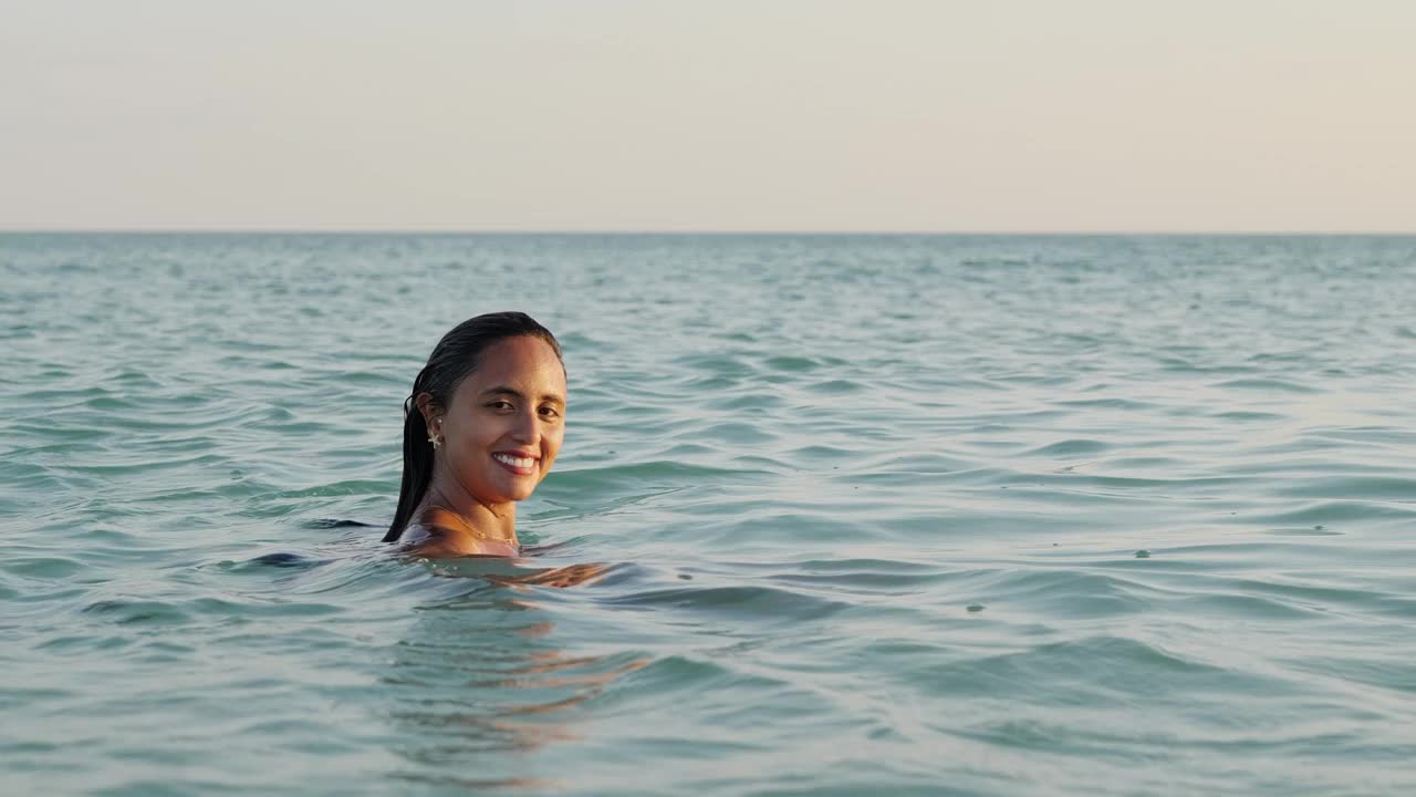 女人看着相机在大海微笑在日落与平静的大海视频素材