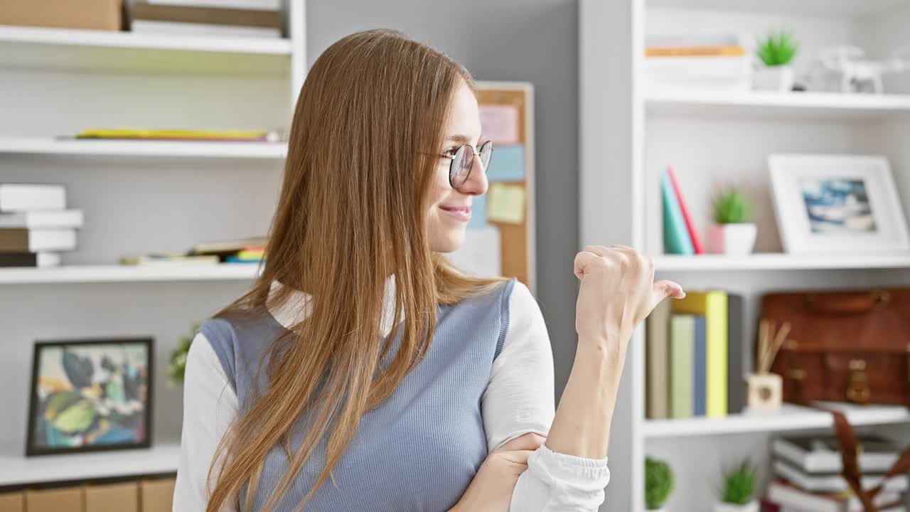 兴奋，自信的年轻金发女商人高兴地指着你和镜头。在舒适的办公室里，她面带积极的微笑。视频素材