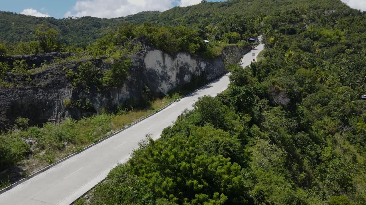 一辆摩托车骑在宿雾岛的乡村公路上，两边是郁郁葱葱的绿色植物，鸟瞰视频素材